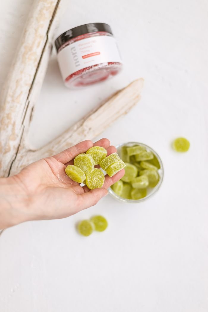 hero-img Close-up of green gummies in hand with a jar in the background on a white surface.